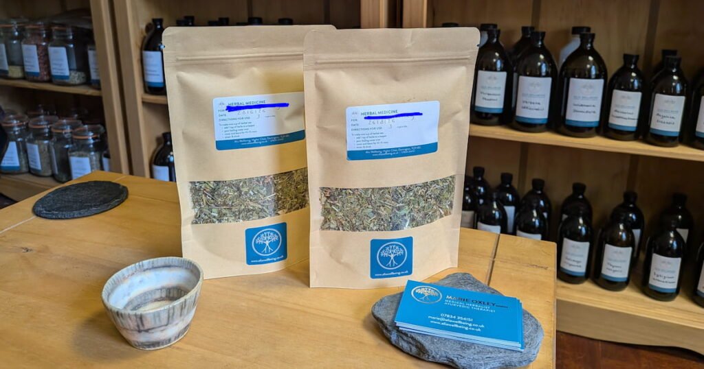 two packets of herbal tea on a table with bottles of tincture in the background